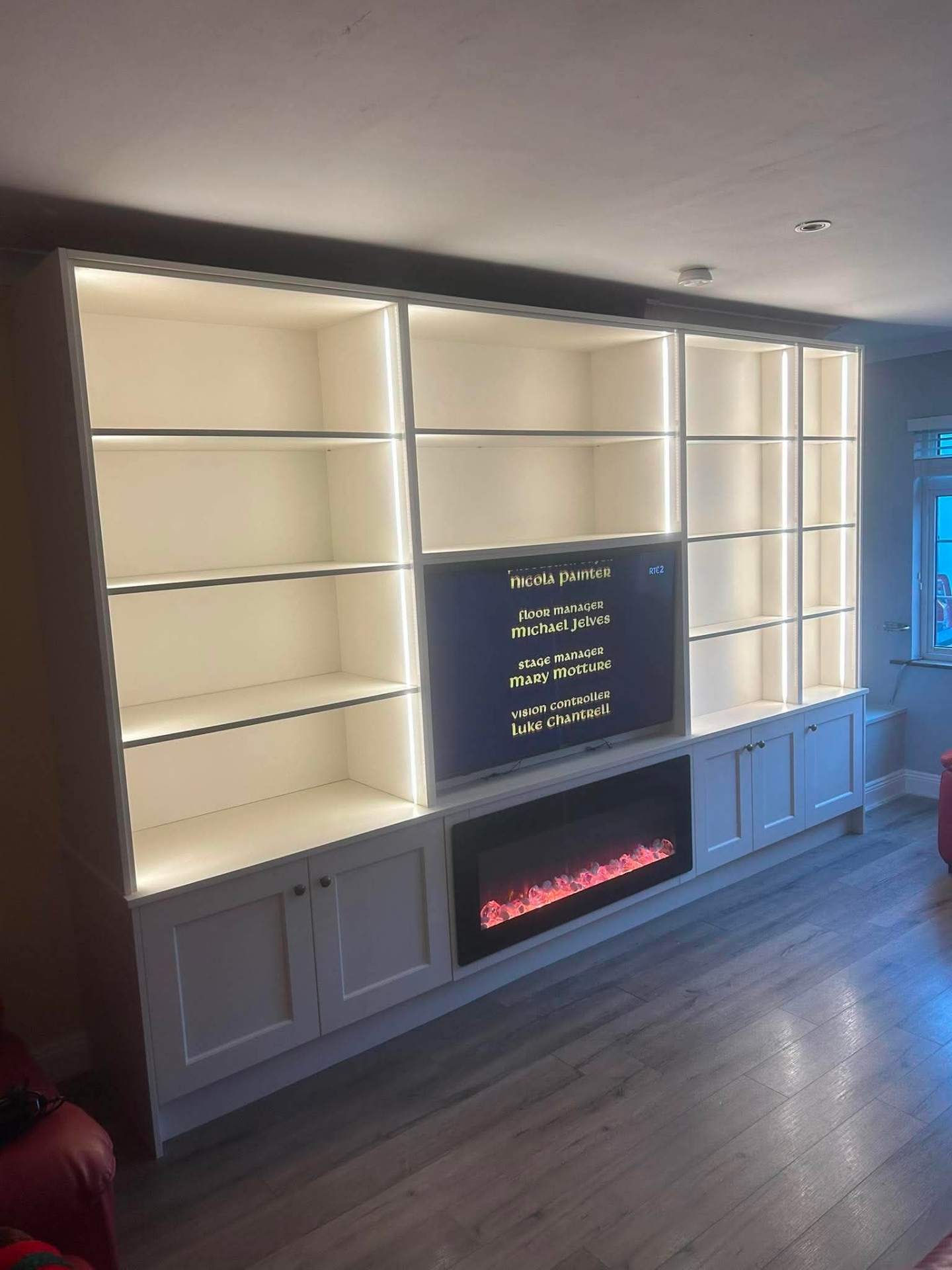 Cream media wall with LED-lit shelving and shaker base cabinets, warm ambient glow