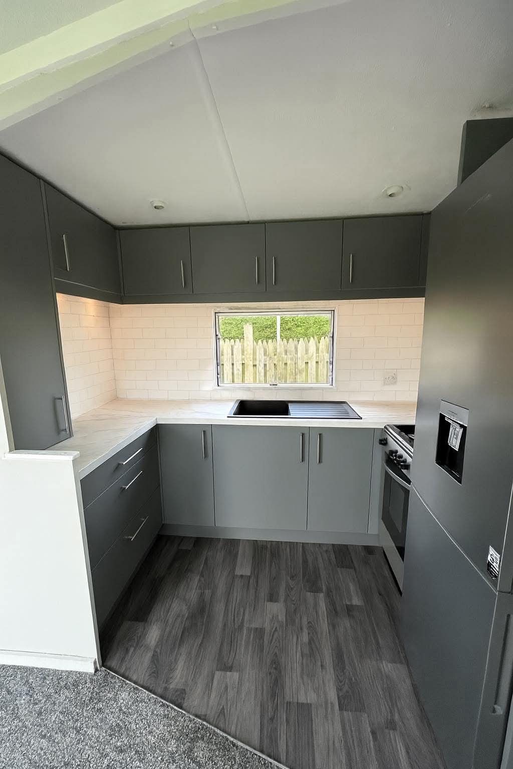 Compact graphite grey kitchen with white stone worktop, subway tile splashback and integrated appliances