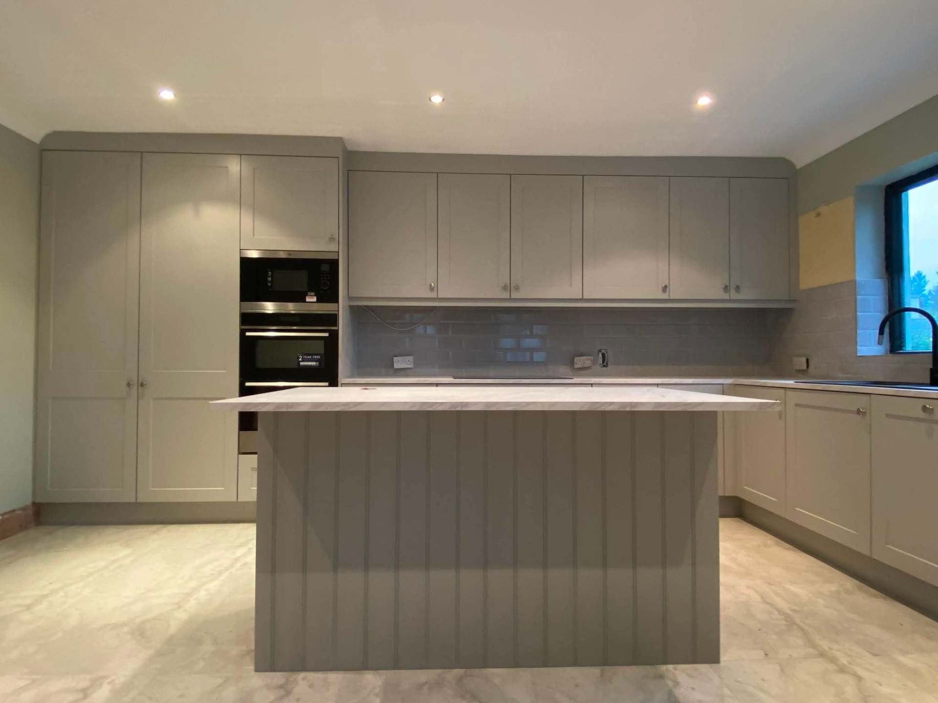 Handpainted grey shaker kitchen with tongue-and-groove island, marble worktop and integrated ovens