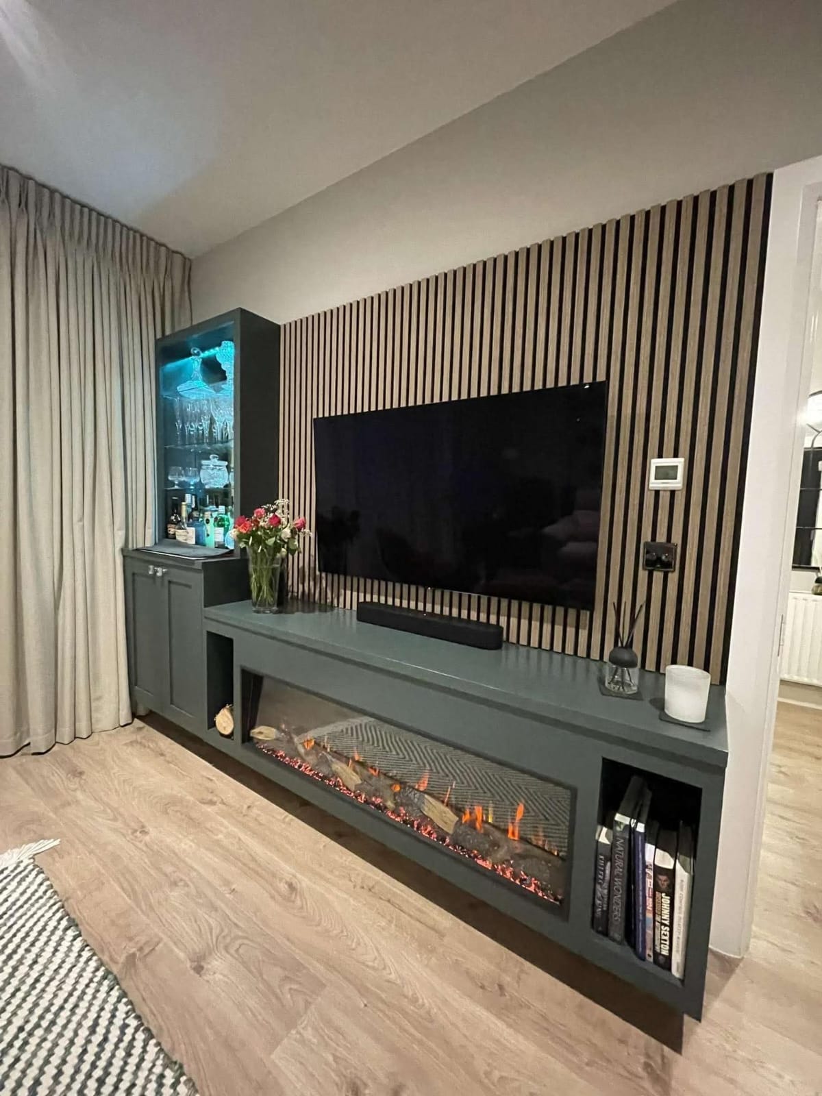 Fluted oak slat wall with dark green floating media unit, linear fire and lit drinks cabinet