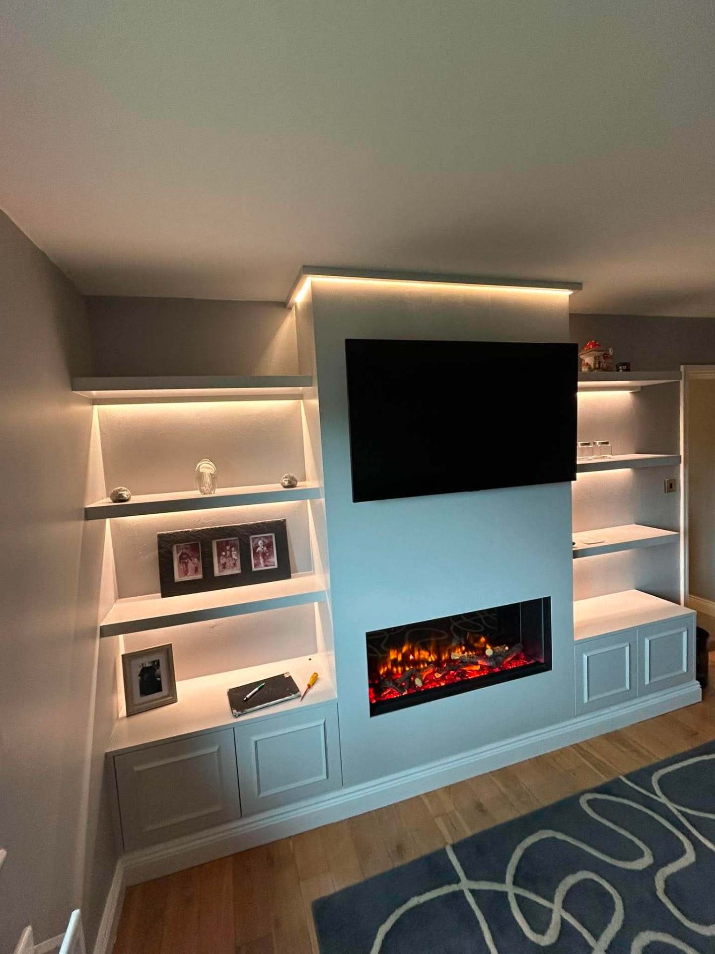 Light blue built-in media wall with LED-lit floating shelves, cabinets and inset electric fire